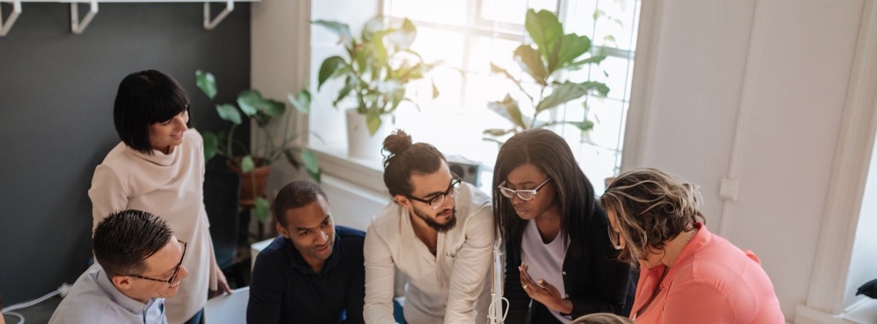 A group of colleagues gathered around a table in a bright office, discussing ideas together.