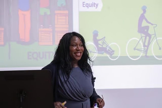 Speaker presenting to an audience with a slide about equity behind her.